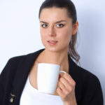 Brunette woman holding cup of coffee and staring at the camera