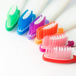 five toothbrushes of various colors lined up next to each other.