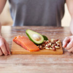 Man sitting in front of salmon, avocado, and nuts on a wooden plate.
