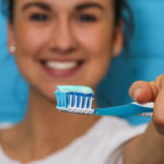 Happy woman holding blue toothbrush with toothpaste up to the camera