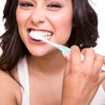 Happy brunette woman in white tank top brushing her teeth