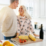 happy older couple preparing a health meal with cheese, tomatoes, bread, and wine