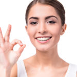 Brunette girl with braces making the OK sign with her hands.