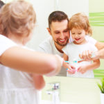 Father helping young daughter brush her teeth