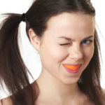 Happy girl with brown hair eating an orange and winking at the camera.