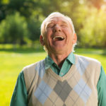 Happy older man in Green shirt laughing in a park.