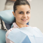 Brunette woman in pink shirt with blue bib at the dentist's office.
