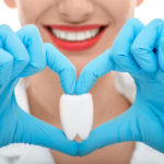 Dental assistant holding model of a tooth with blue gloves.