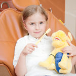 Small happy girl with stuffed animal holding a toothbrush at the dentist's